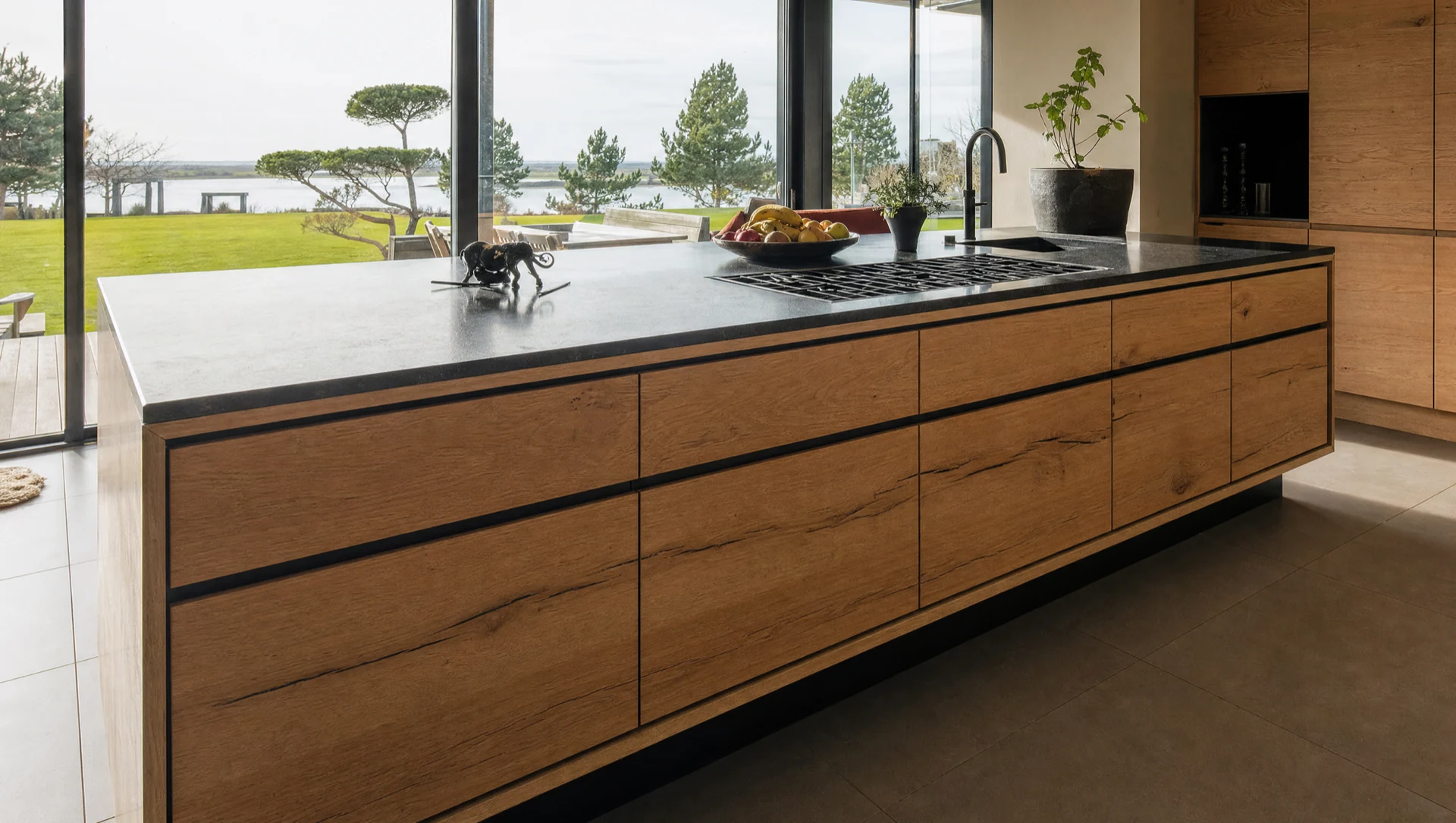 The dark run of tall units and base cabinets, with a patinated metal panel behind the range