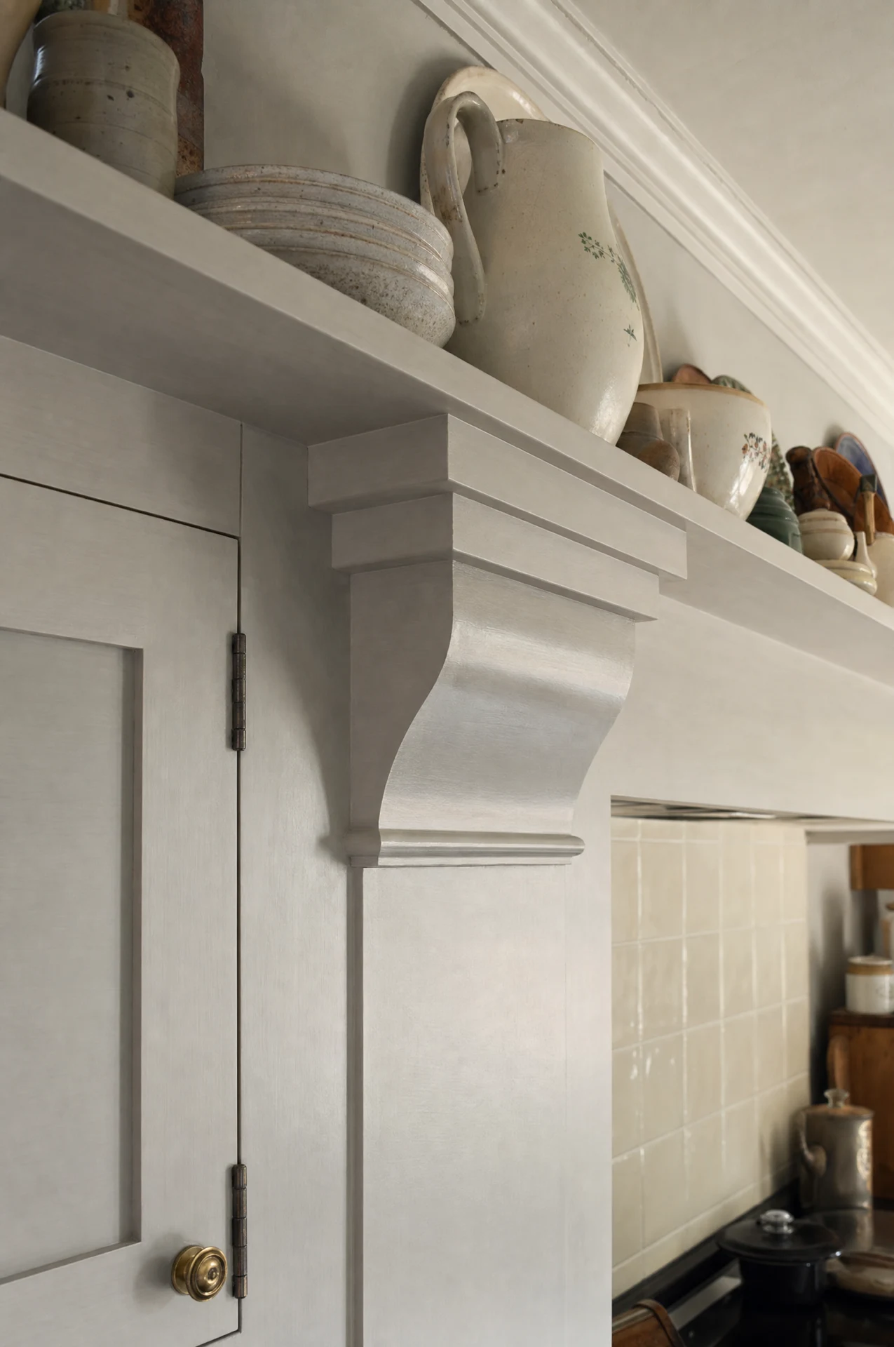 A molded bracket carrying the plate shelf over a wall cabinet, with jugs and bowls above and cream tiles behind